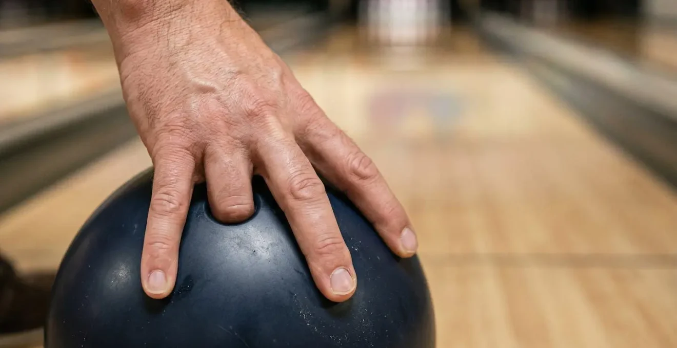 Main de joueur de bowling au moment précis du lâcher de boule, doigts en extension pour créer la rotation, mise au point sur la gestuelle technique