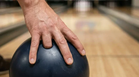 Main de joueur de bowling au moment précis du lâcher de boule, doigts en extension pour créer la rotation, mise au point sur la gestuelle technique