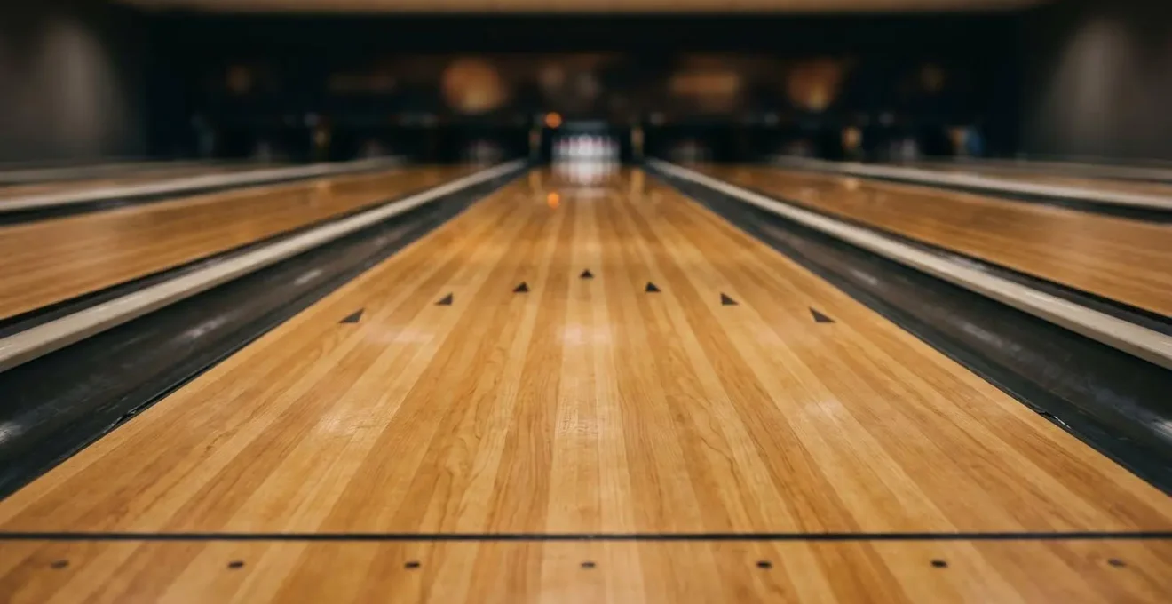 Vue détaillée d'une piste de bowling montrant les lattes en bois et les flèches de visée sous un éclairage naturel