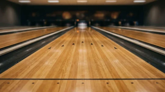 Vue détaillée d'une piste de bowling montrant les lattes en bois et les flèches de visée sous un éclairage naturel